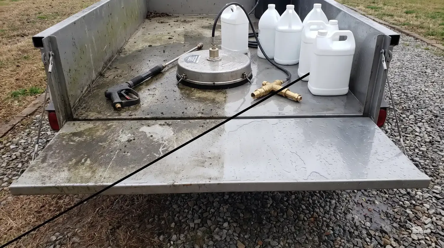 Photograph-style spray wand, two surface-cleaner discs, a brass injector and plain white jugs on a steel trailer bench whose deck is grimed on one side of the diagonal and wiped clean on the other