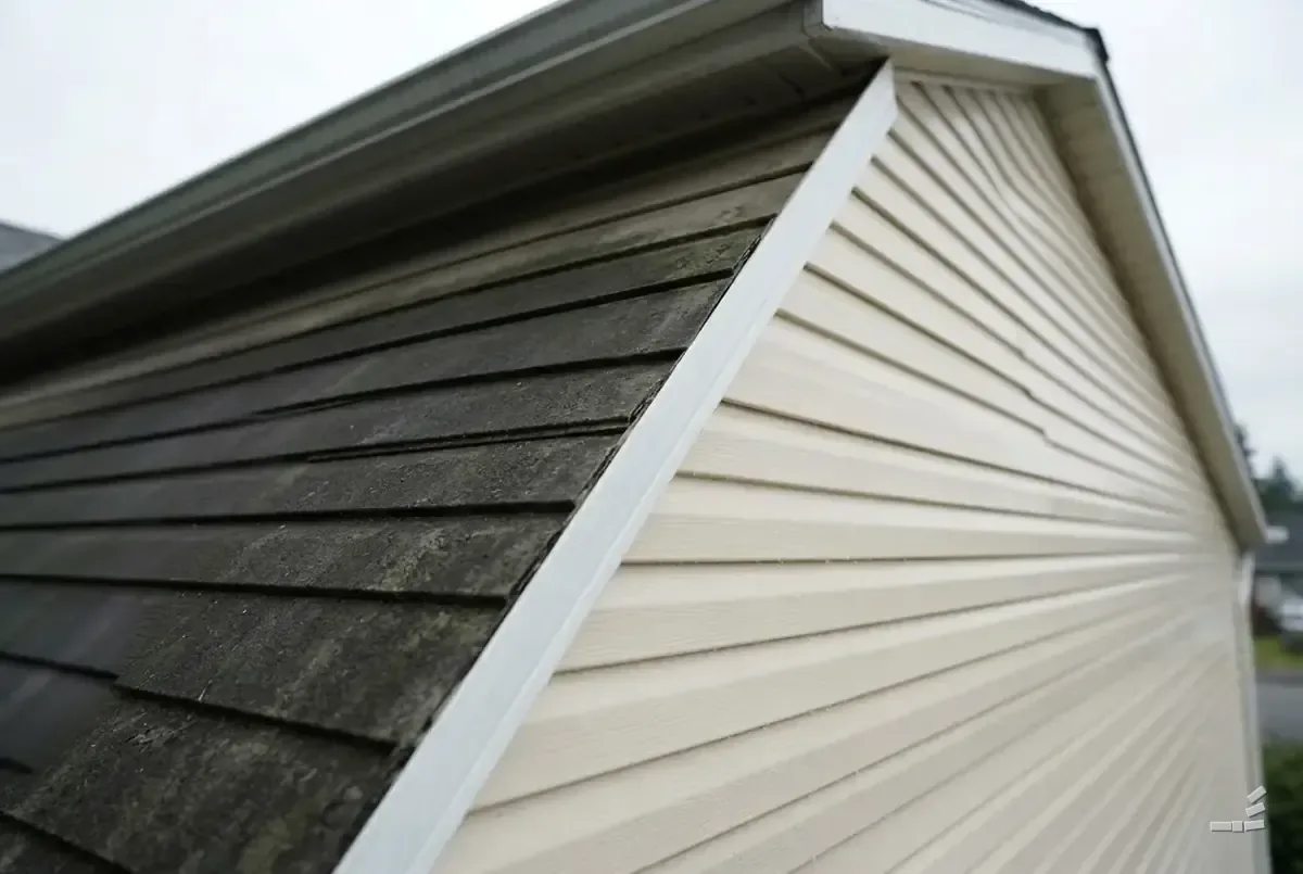 Photograph-style gable split along one diagonal between dark weathered shingle siding and bare clean cream vinyl