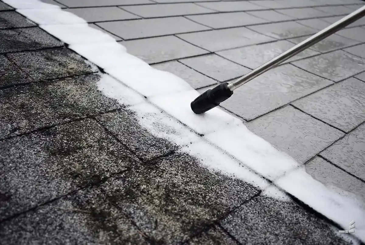 Photograph-style soft-wash nozzle laying foam across algae-streaked shingles