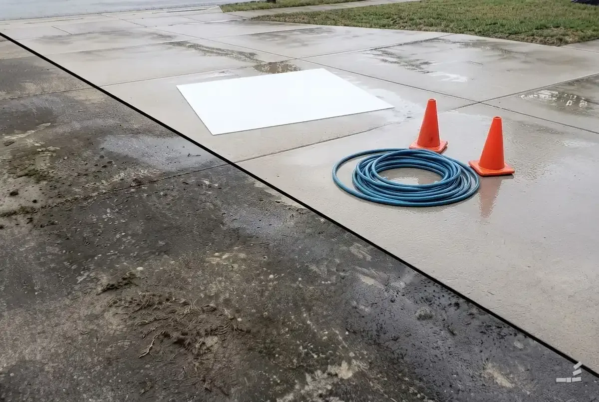 Photograph-style blank sheet, a coiled hose and two cones on the clean half of a concrete drive, mossy concrete below the diagonal